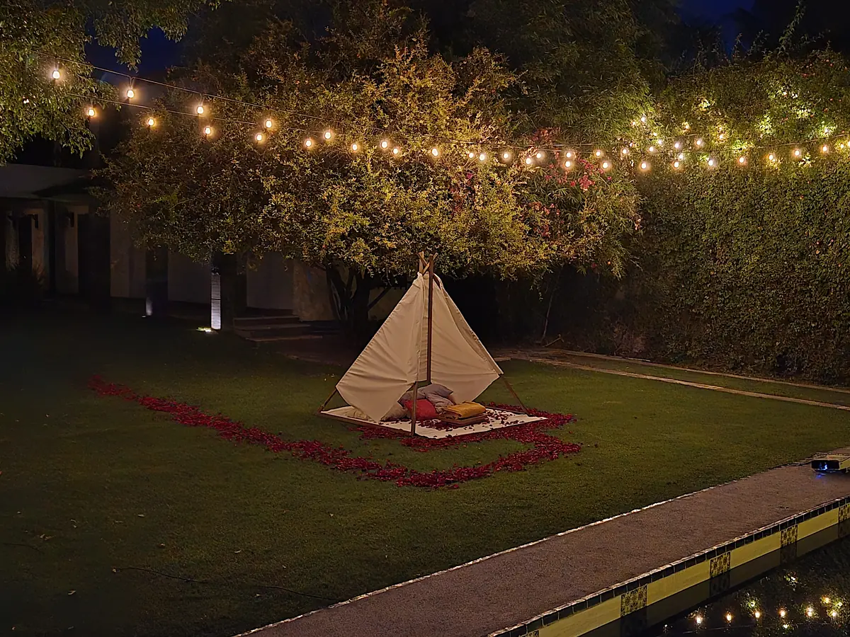 El jardín de noche con focos colgantes y el teepee del cine junto a la alberca