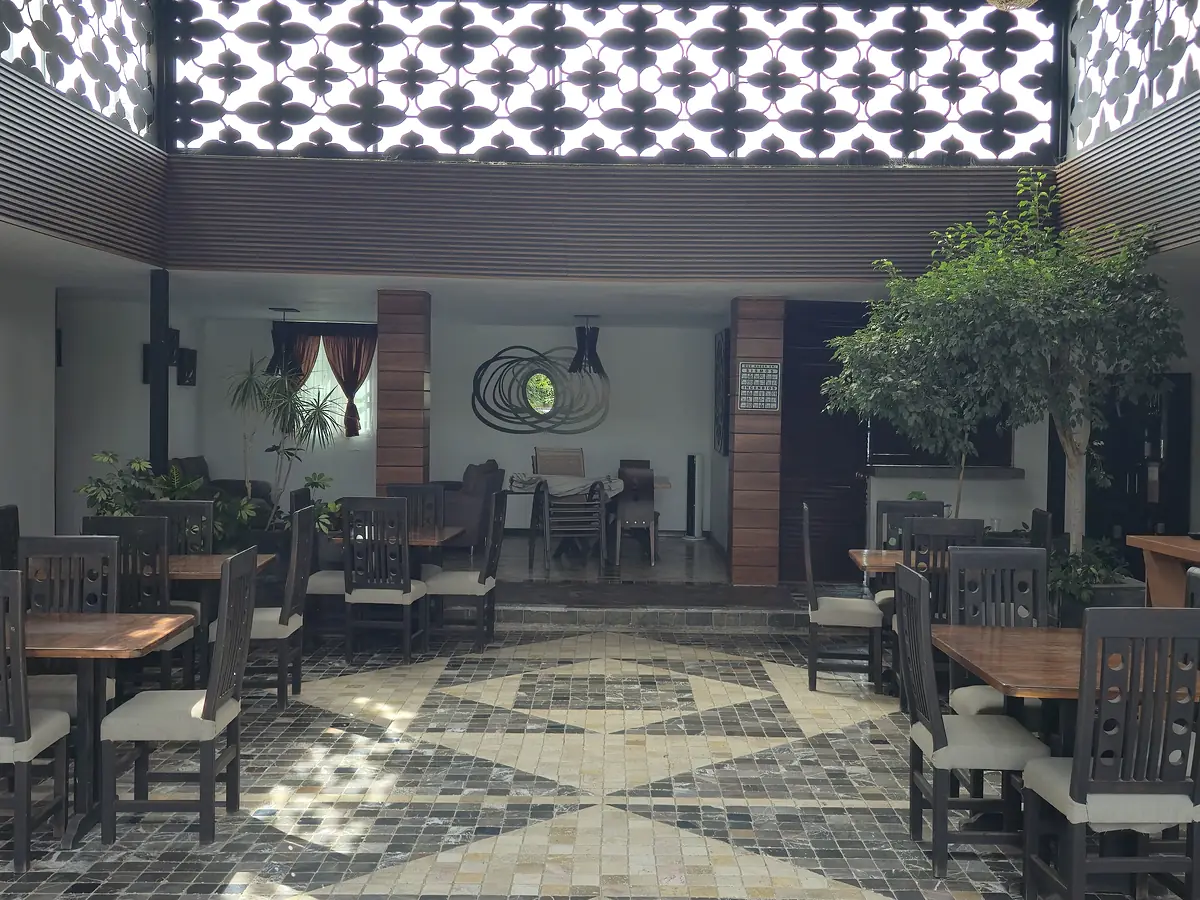El patio techado con celosía, mesas de madera y piso de mosaico